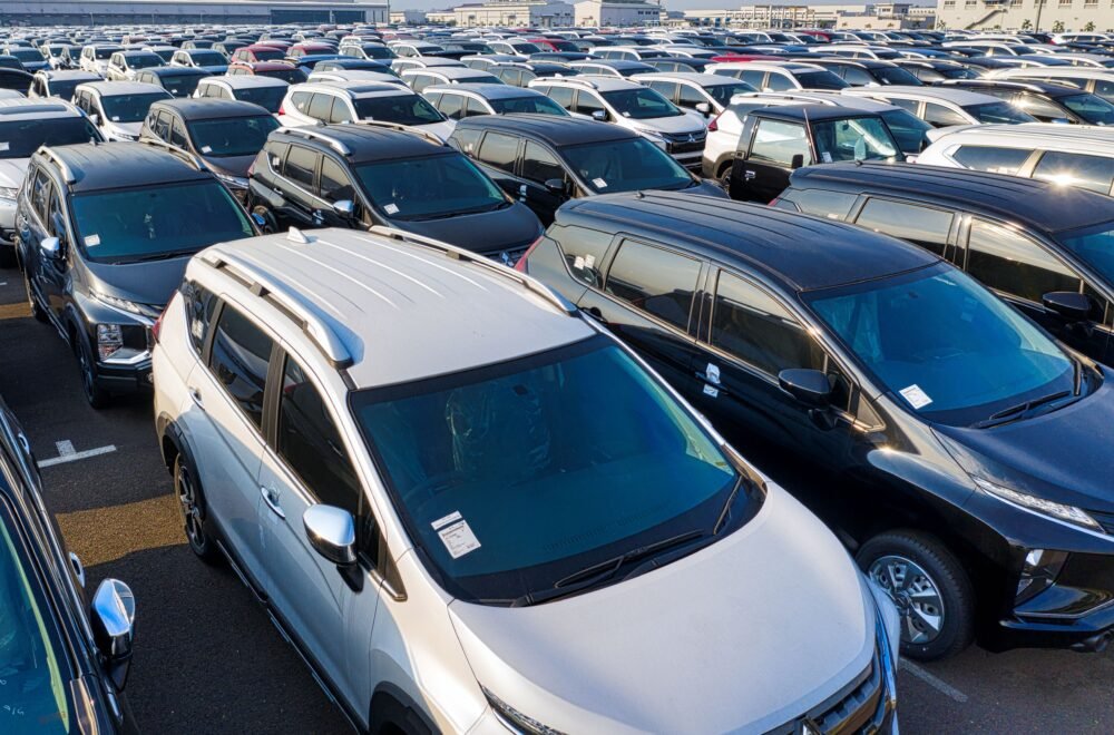 Modern sparkling clean new automobiles on asphalt parking near factory of manufacture in daytime